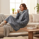 Grey fleece hooded blanket with teddy bear embroidery worn relaxing on a sofa with a warm drink