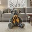 Charcoal grey teddy bear with a tan muzzle and ear patches, wearing a mustard satin bow at its neck