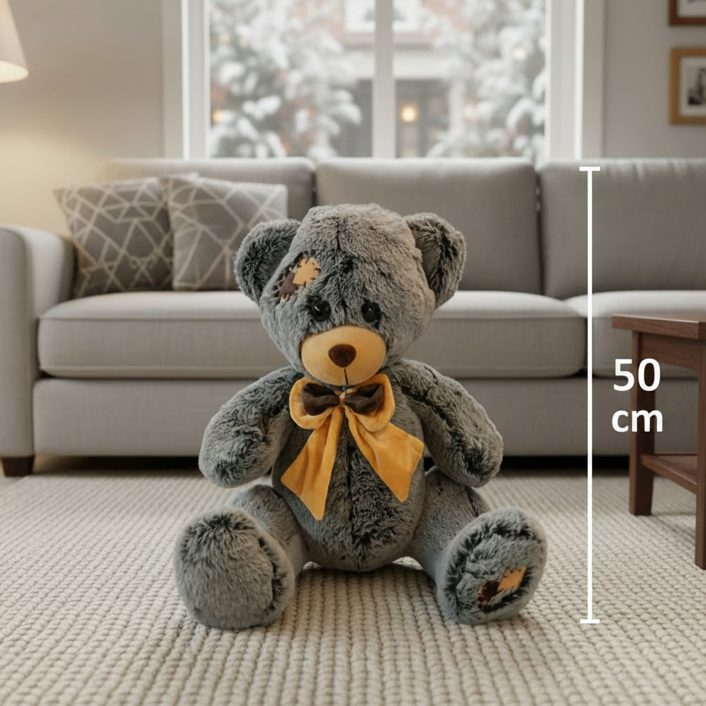 Charcoal grey teddy bear with a tan muzzle and ear patches, wearing a mustard satin bow at its neck