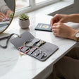 Grey travel jewelry roll opened flat on a marble table with rings and bracelets held in elastic loops