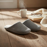 Pair of grey waffle knit slippers on a sunlit wood floor beside a book