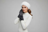 Woman wearing a white sweater, fur hat, and grey leather gloves on a light grey background