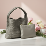 Woven handbag and matching pouch on a light surface with flowers and a cup in the background