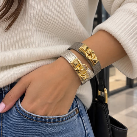 Woman wearing grey and metallic silver wrap bracelets with gold pyramid studs, stacked on her wrist with a cream sweater