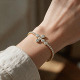 Gold halo cross tennis bracelet worn with a linen sleeve on a sunny wooden table