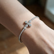 Silver tennis bracelet with a halo crystal cross worn on a raised wrist by a window