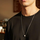 Halo cylinder pendant necklace worn over a black tee in a warm cafe