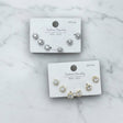 Set of gold and silver halo stud earrings on branded cards against a marble background