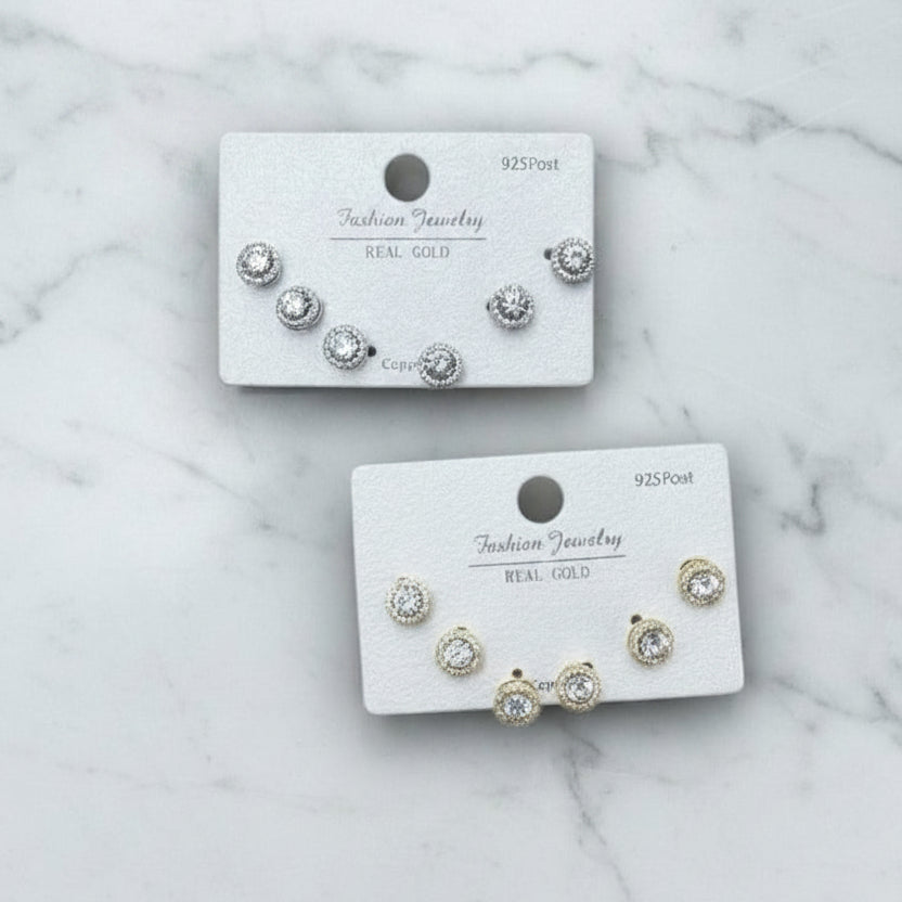 Set of gold and silver halo stud earrings on branded cards against a marble background