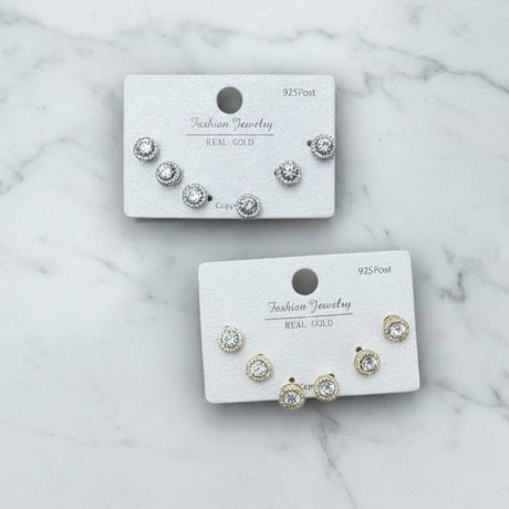 Set of gold and silver halo stud earrings on branded cards against a marble background