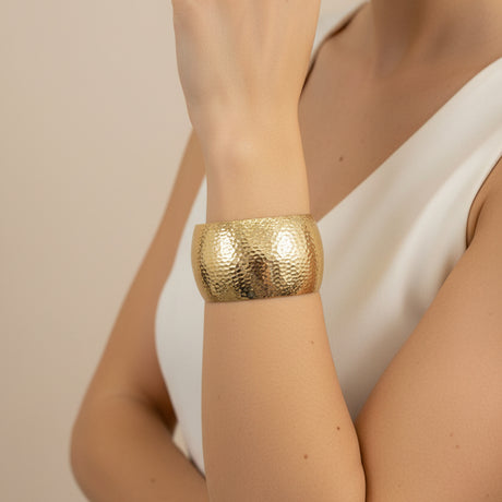 Hammered gold cuff bracelet on a wrist on a beige background