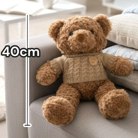 Caramel boucle bear in a sand cable knit jumper sitting against stacked cushions