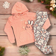 Pink hooded pyjama set with bunny-print pants displayed on a wooden surface with decorative accents