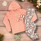 Pink hooded pyjama set with bunny-print pants displayed on a wooden surface with decorative accents