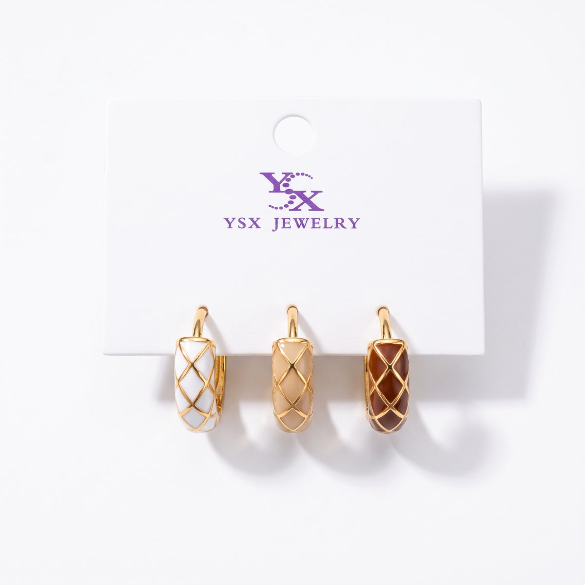Three single harlequin enamel huggie earrings in white, beige and brown with gold lines