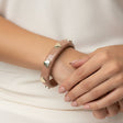 Person wearing a pink bracelet with heart-shaped charms on a light background