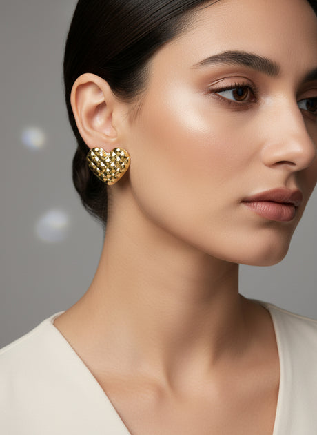 Close-up of a woman wearing gold heart-shaped earrings against a neutral background