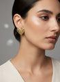 Close-up of a woman wearing gold heart-shaped earrings against a neutral background