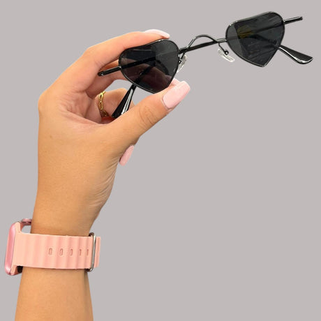 Hand holding a pair of heart-shaped sunglasses with a grey background