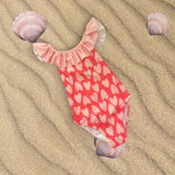 Coral heart print swimsuit flat lay on sand