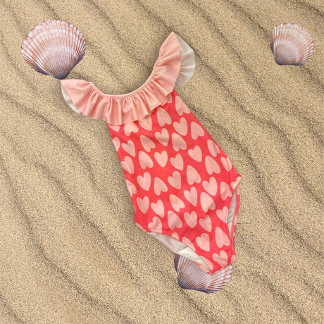 Coral heart print swimsuit flat lay on sand