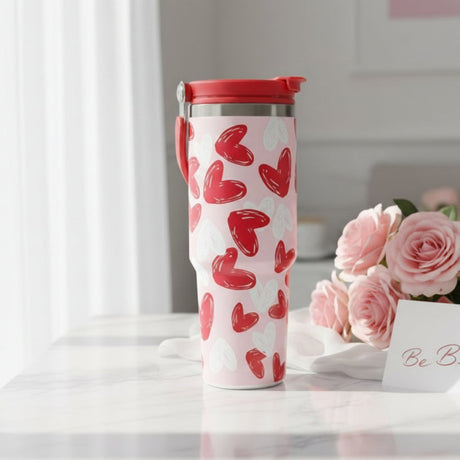 Pale pink travel mug with bold red and white brush stroke hearts and a red lid