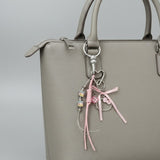 Grey handbag with a decorative keychain featuring pink ribbons and a Hello Kitty charm on a grey background