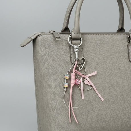 Grey handbag with a decorative keychain featuring pink ribbons and a Hello Kitty charm on a grey background