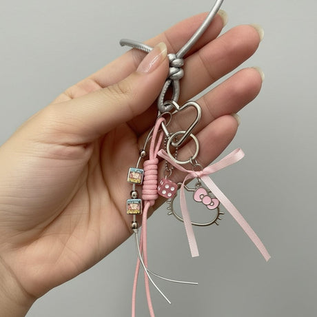 Hand holding a decorative keychain with pink ribbon and Hello Kitty charm against a grey background