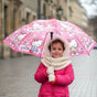 Girl in a pink coat holding an open coral pink Hello Kitty kids umbrella