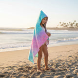 Girl on the beach in a rainbow ombre mermaid scale hooded towel wrap with teal starfish