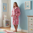 Young girl wearing a pink robe with cartoon characters in a room with light blue walls and a unicorn toy