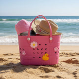 Pink crocs bag with a straw hat, and towel set on the beach.