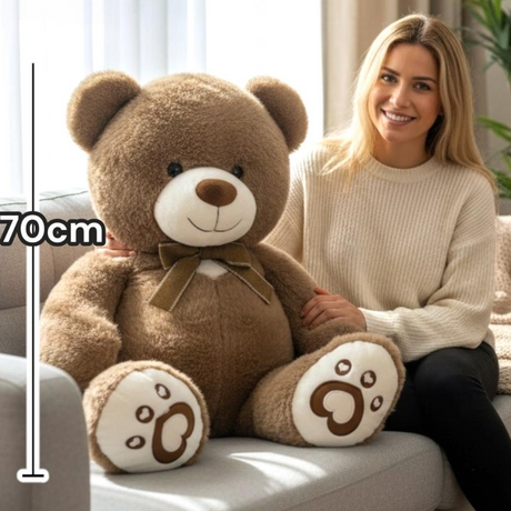 Tan huggable teddy bear with an olive ribbon bow seated beside a woman