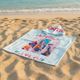 Towel with colorful graphics and text on a sandy beach with ocean in the background