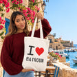 Woman holding up a cream I love Batroun canvas tote with the old harbour behind her