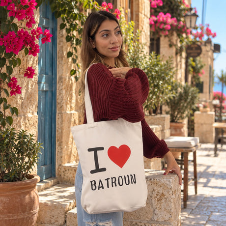Cream canvas tote printed I love Batroun with a red heart, worn on the shoulder by a stone wall