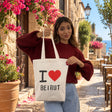 Woman holding a cream I love Beirut canvas tote by its long handles on a flower lined street