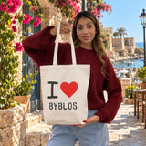 Woman holding a cream I love Byblos canvas tote with a red heart in an old stone street