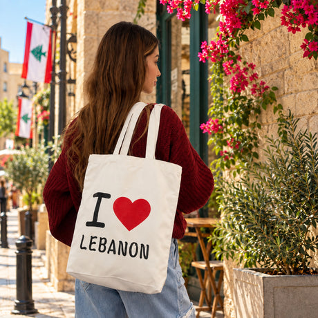 Back view of a cream I love Lebanon canvas tote worn on the shoulder in a flower lined alley