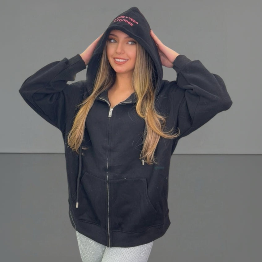 Woman wearing a black zip jacket with text on the hood against a grey background
