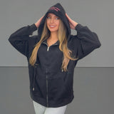 Woman wearing a black zip jacket with text on the hood against a grey background