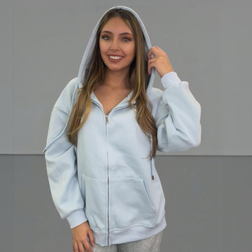 Woman wearing a light blue zip jacket with a hood against a grey background