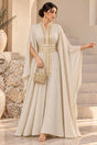 Woman in an ivory cape sleeve kaftan with a gold embroidered belt, standing on stone steps