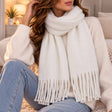 Ivory blanket scarf worn over a cream knit with long twisted tassel ends
