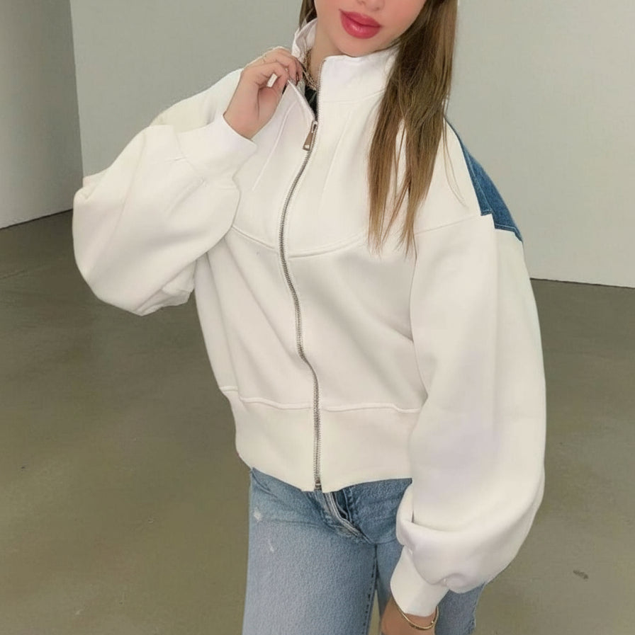 Person wearing a white zip-up sweatshirt jacket and light blue jeans indoors
