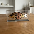 The word Jesus formed as a fish, each letter a different mirrored metal, on an oak table