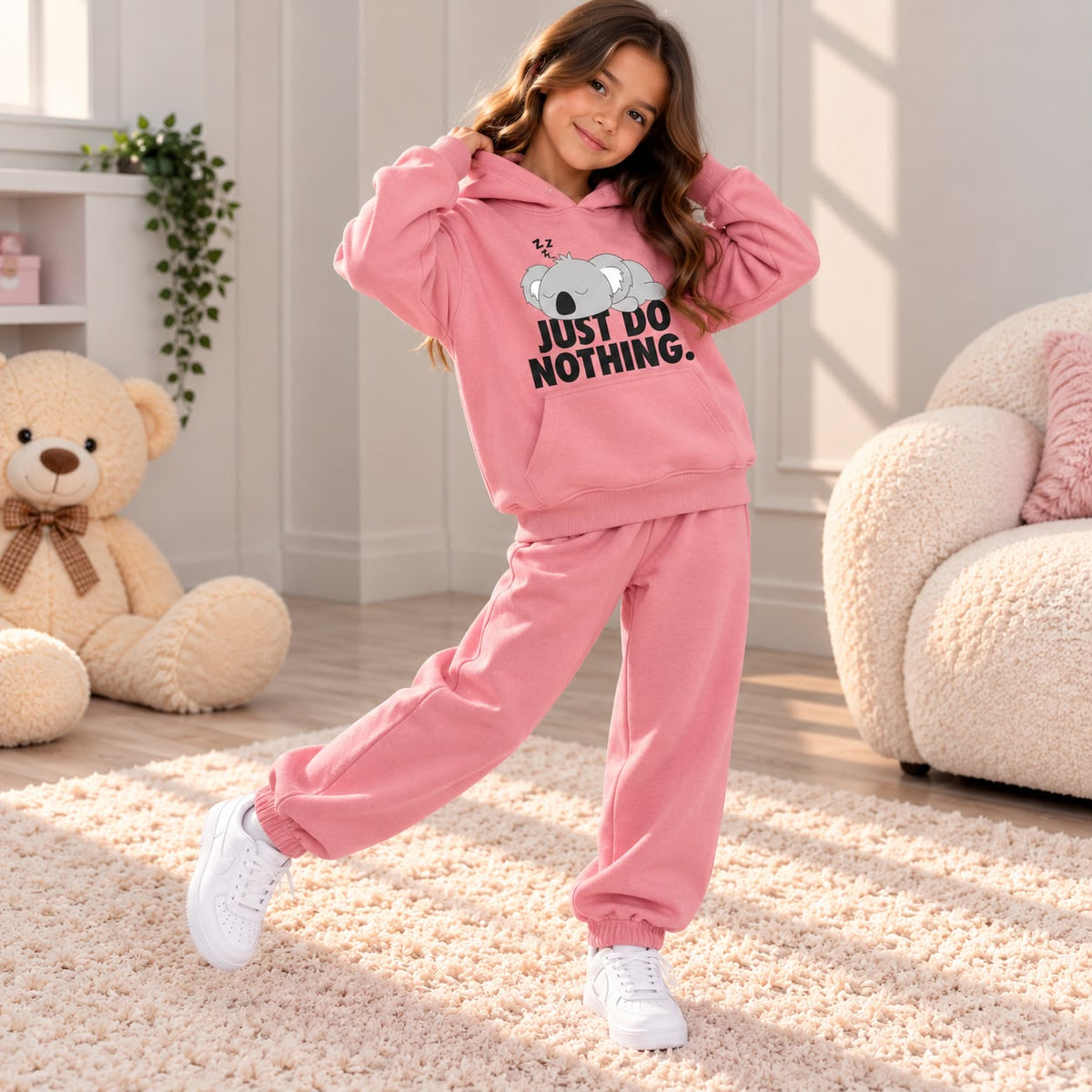 Girl in a dusty pink koala slogan hoodie and matching pink joggers on a cream rug