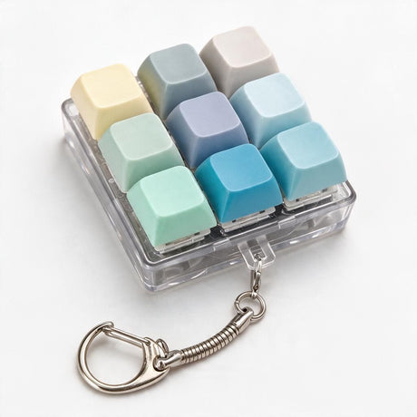 Keycap clicker keychain with mixed yellow, sage, grey, blue and mint keys in a clear case