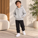 Boy in a light grey zip up hoodie and black joggers with white trainers, hands in pockets